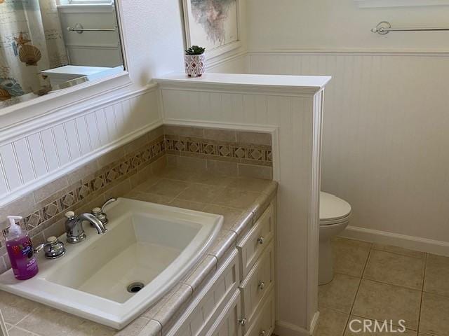 bathroom with toilet, wainscoting, vanity, decorative backsplash, and tile patterned flooring
