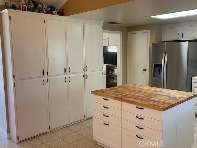 kitchen with stainless steel fridge with ice dispenser, light tile patterned floors, white cabinets, and butcher block counters