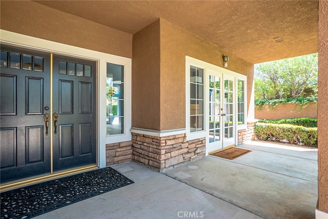 entrance to property featuring french doors, stucco siding, and stone siding