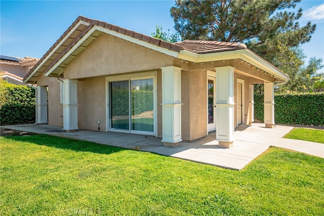 rear view of house featuring a patio area, stucco siding, a lawn, and a tile roof