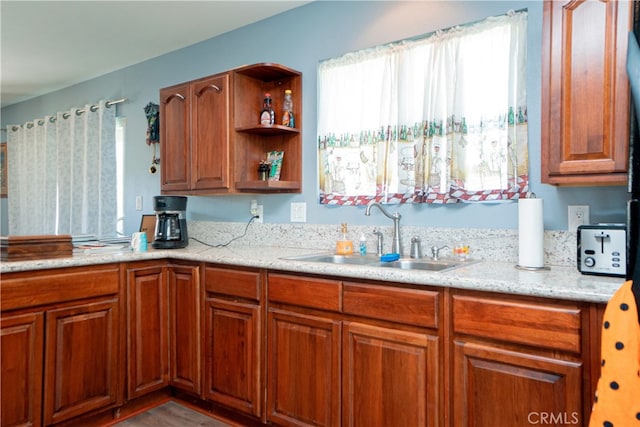 kitchen featuring open shelves, wood finished floors, light stone counters, a sink, and brown cabinets