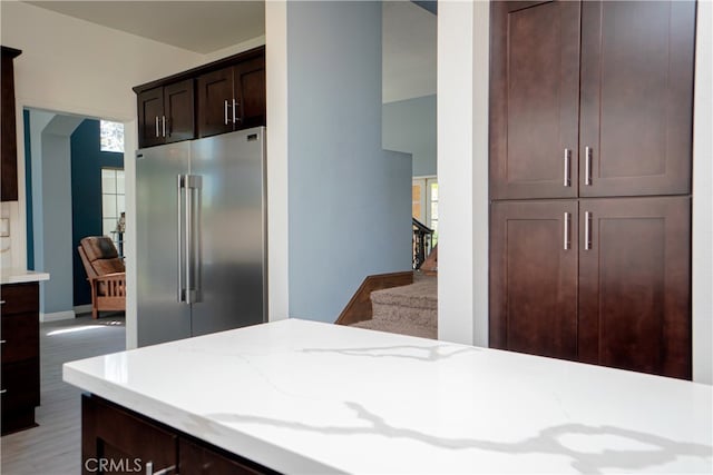 kitchen with baseboards, high end fridge, dark brown cabinets, light stone countertops, and light wood finished floors