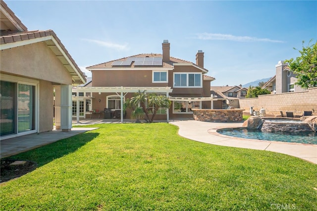 back of house featuring solar panels, a patio area, a lawn, a chimney, and stucco siding
