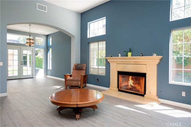 sitting room with a glass covered fireplace, a towering ceiling, visible vents, arched walkways, and wood finished floors