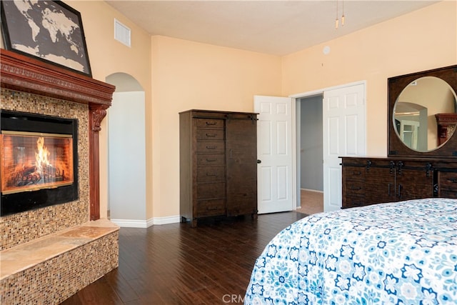 bedroom featuring visible vents, baseboards, arched walkways, a fireplace, and wood finished floors