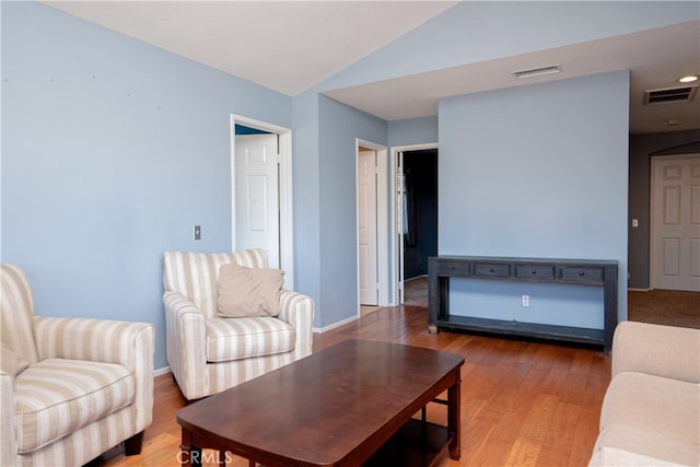 living room featuring lofted ceiling, visible vents, baseboards, and wood finished floors