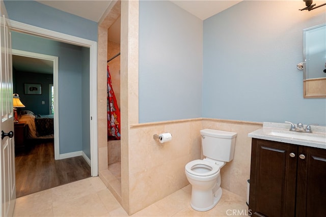 full bath featuring vanity, a wainscoted wall, a tile shower, and toilet