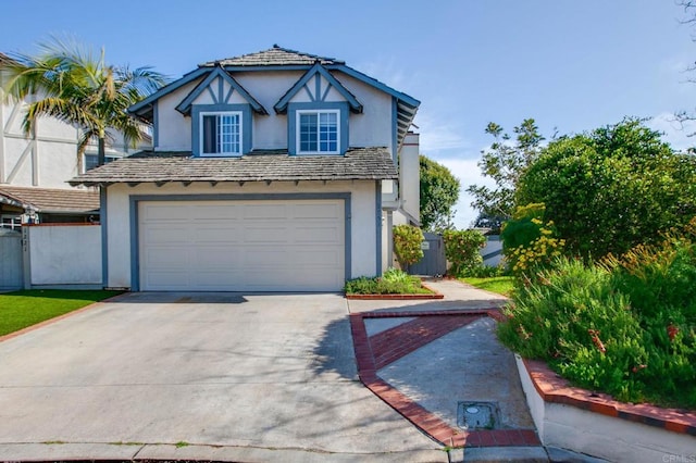 tudor home with stucco siding, a garage, concrete driveway, and fence