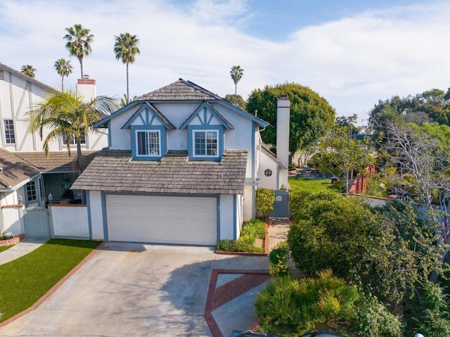 tudor house featuring driveway, an attached garage, stucco siding, fence, and a chimney