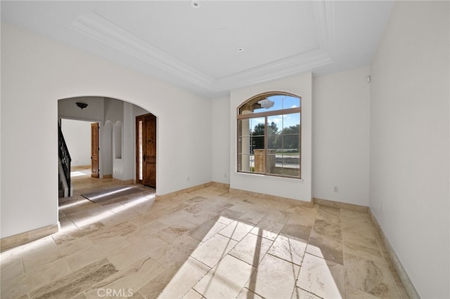 spare room featuring arched walkways, stone tile flooring, ornamental molding, baseboards, and a tray ceiling