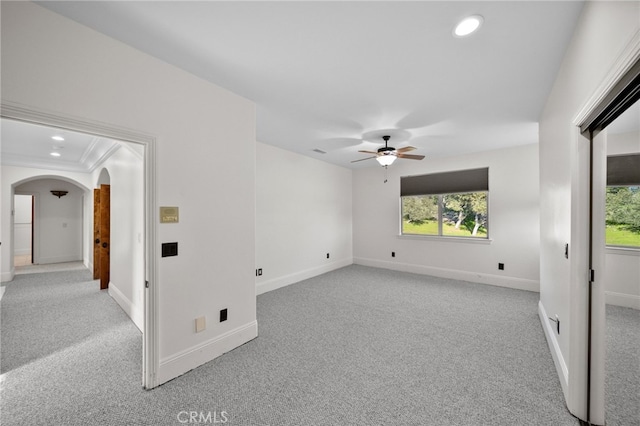 empty room featuring arched walkways, ceiling fan, and light carpet