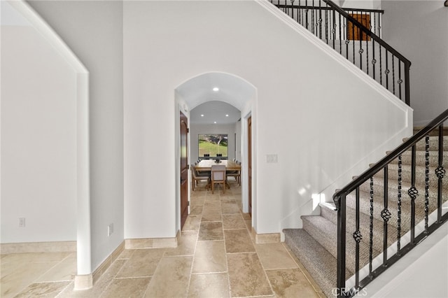 entrance foyer with baseboards, stairway, arched walkways, and stone tile flooring