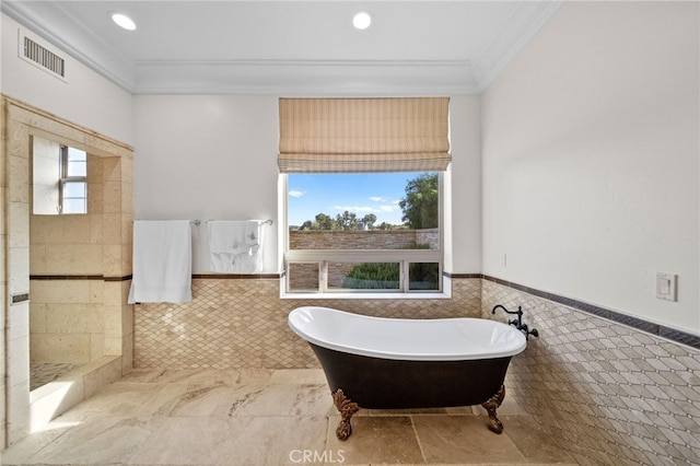 bathroom with tile walls, a wainscoted wall, a soaking tub, visible vents, and crown molding