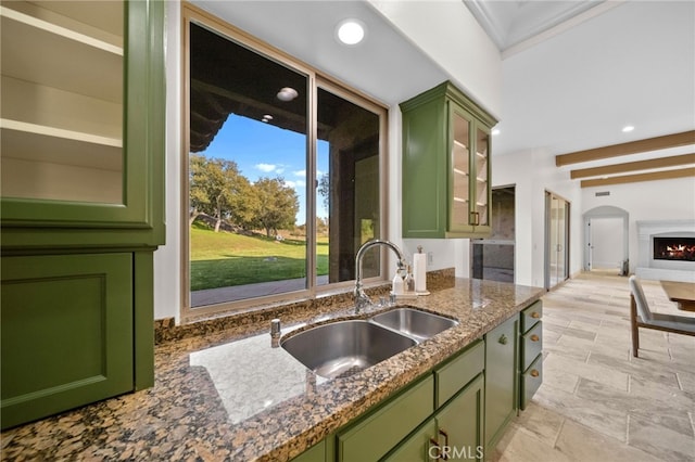 kitchen with dark stone countertops, recessed lighting, arched walkways, green cabinetry, and a sink