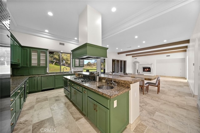 kitchen featuring an island with sink, island range hood, green cabinetry, built in appliances, and a sink