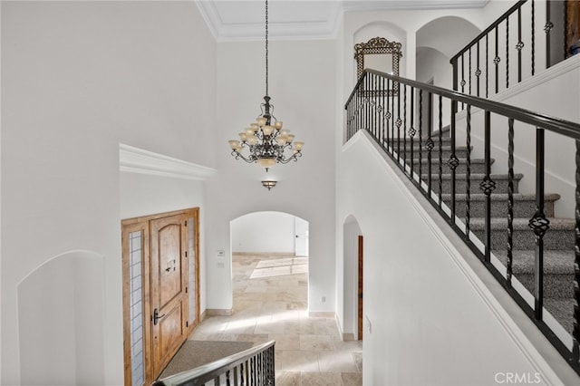 interior space with arched walkways, a chandelier, ornamental molding, baseboards, and a high ceiling