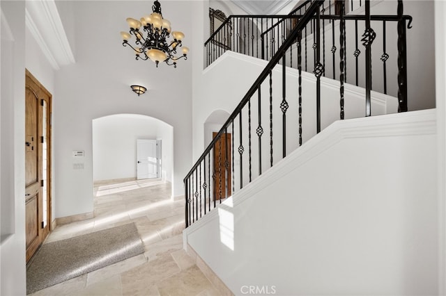 stairs featuring arched walkways, baseboards, a notable chandelier, a high ceiling, and crown molding