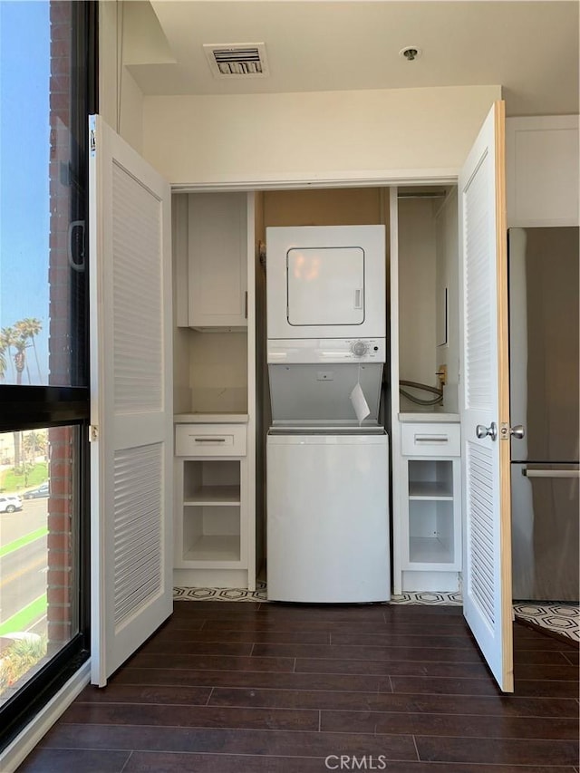 laundry room with dark wood-style floors, laundry area, stacked washer / drying machine, and visible vents