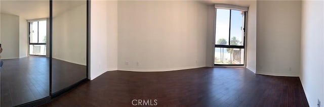 empty room with dark wood-type flooring, a wealth of natural light, and baseboards
