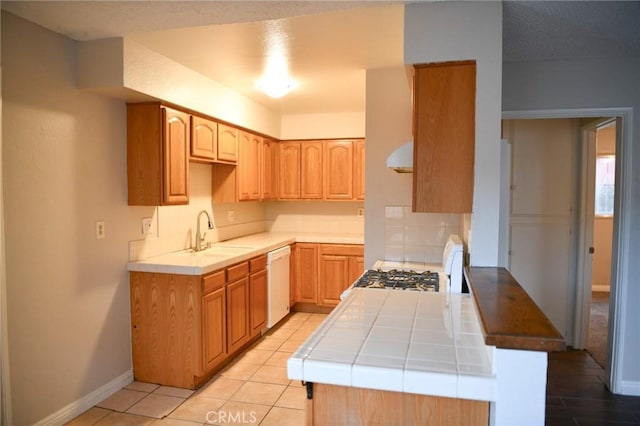 kitchen with dishwasher, tile counters, a sink, and extractor fan