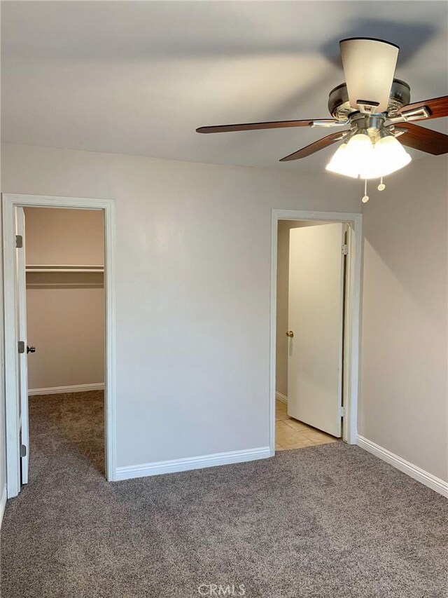 unfurnished bedroom featuring a ceiling fan, light carpet, baseboards, and a spacious closet