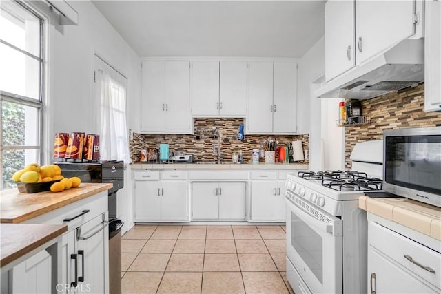 kitchen featuring stainless steel microwave, gas range gas stove, under cabinet range hood, tile countertops, and a sink