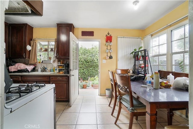kitchen featuring light tile patterned flooring, decorative backsplash, a sink, and gas range gas stove