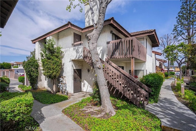 back of house featuring stairway, stucco siding, and a tiled roof