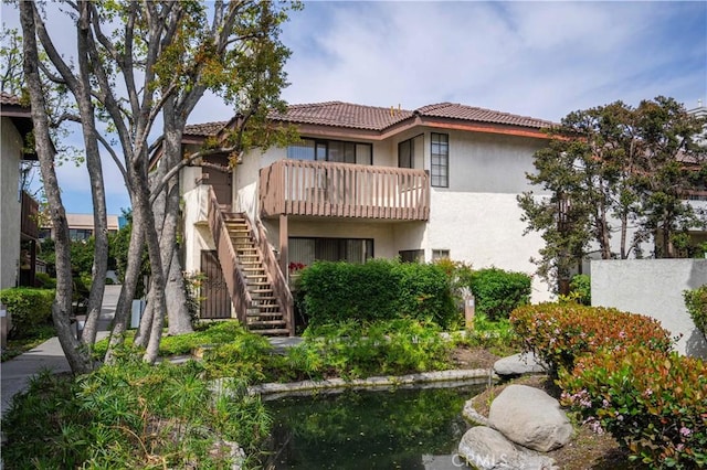 rear view of house featuring a balcony, stairway, stucco siding, and a tiled roof