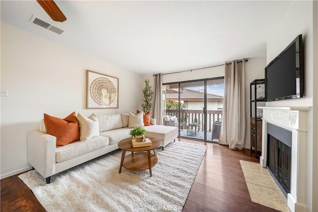 living area with a ceiling fan, a fireplace with flush hearth, visible vents, and wood finished floors