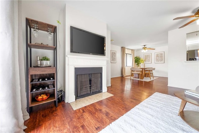 living area with a fireplace with flush hearth, wood finished floors, and ceiling fan
