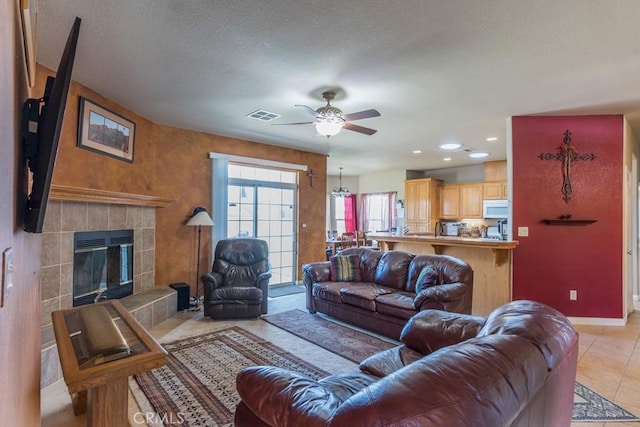 living area featuring baseboards, a tiled fireplace, light tile patterned floors, a ceiling fan, and visible vents