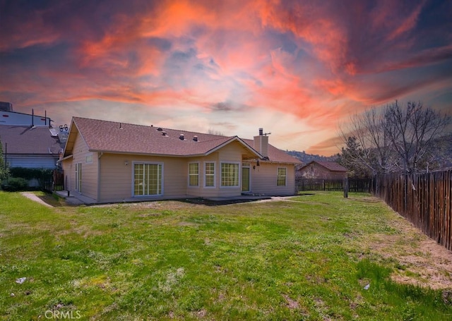 back of property at dusk featuring a yard, a fenced backyard, and a chimney