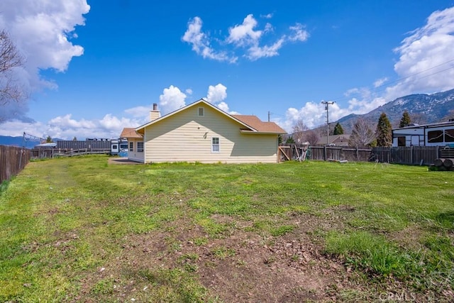 rear view of house featuring a mountain view, a fenced backyard, a chimney, and a lawn