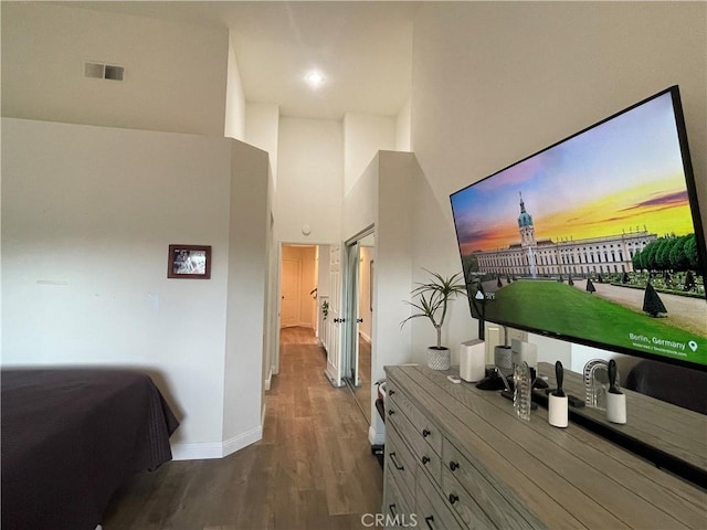 bedroom featuring visible vents, a towering ceiling, baseboards, and wood finished floors