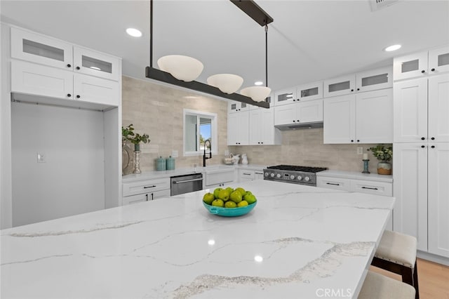 kitchen with backsplash, white cabinets, light stone countertops, and stainless steel appliances