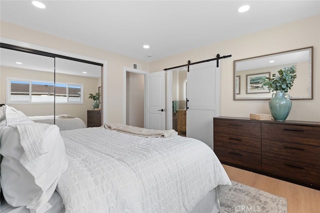 bedroom with a closet, recessed lighting, a barn door, light wood-style floors, and visible vents