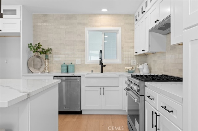 kitchen with glass insert cabinets, a sink, under cabinet range hood, white cabinetry, and stainless steel appliances