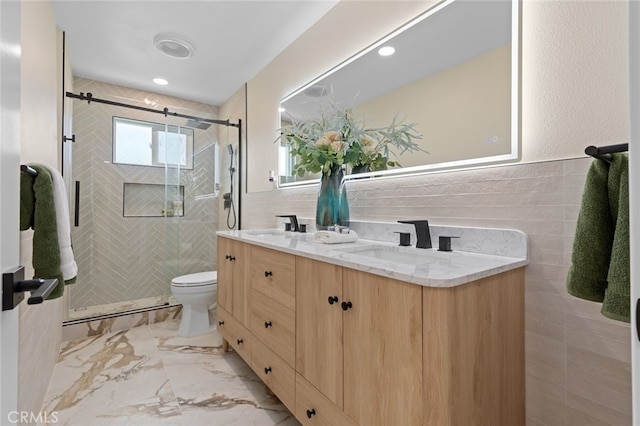bathroom featuring a shower stall, double vanity, a sink, and tile walls