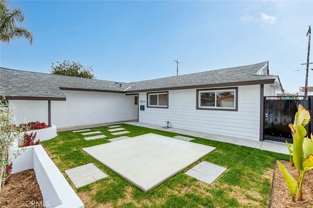 rear view of house featuring a patio, roof with shingles, a yard, and fence