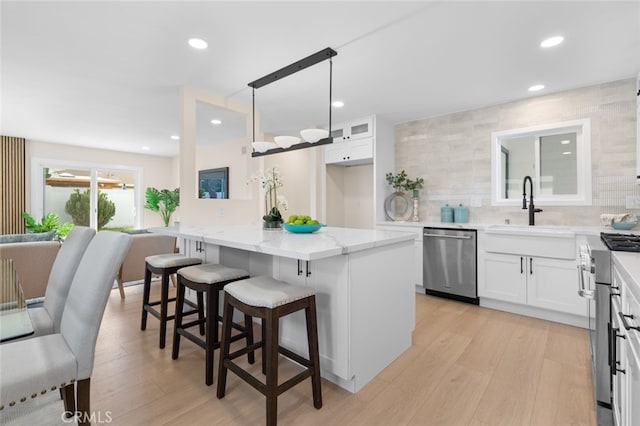 kitchen with stainless steel dishwasher, light stone countertops, white cabinetry, a breakfast bar, and a sink
