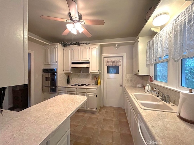 kitchen with oven, a sink, light countertops, under cabinet range hood, and backsplash