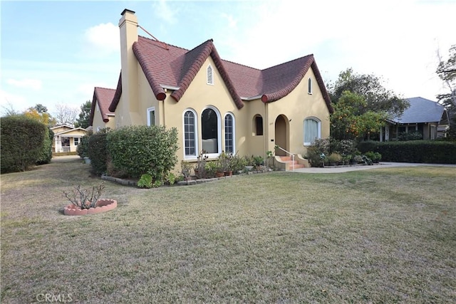tudor house featuring a front yard, a chimney, and stucco siding