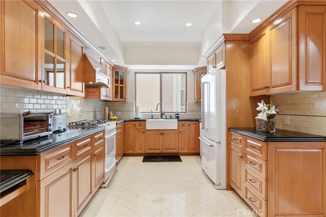 kitchen with decorative backsplash, a sink, white appliances, and glass insert cabinets