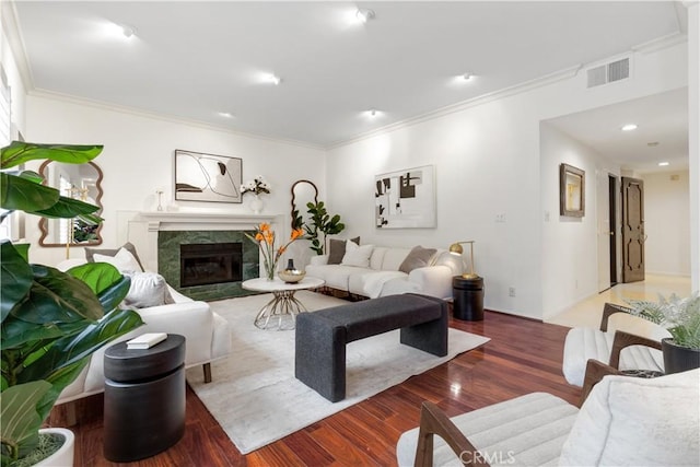 living area with visible vents, a high end fireplace, wood finished floors, and ornamental molding