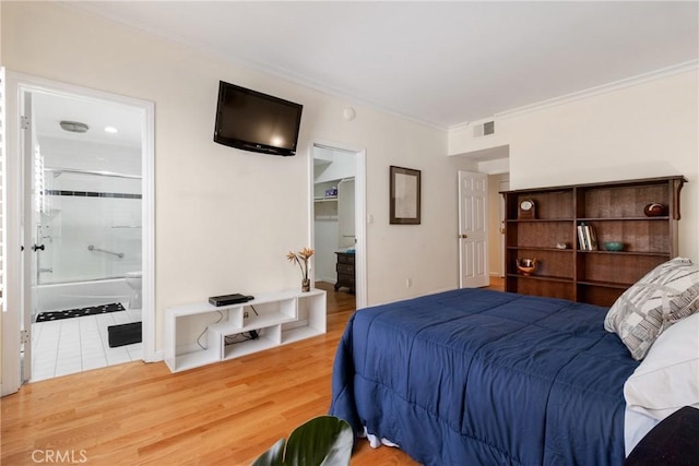 bedroom featuring visible vents, a spacious closet, wood finished floors, crown molding, and ensuite bath