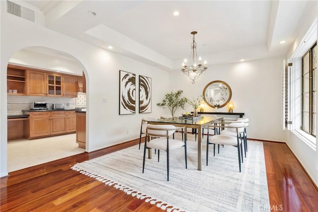 dining area featuring arched walkways, light wood-style flooring, visible vents, and a tray ceiling