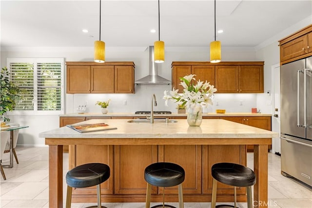 kitchen featuring brown cabinetry, light countertops, appliances with stainless steel finishes, and wall chimney exhaust hood