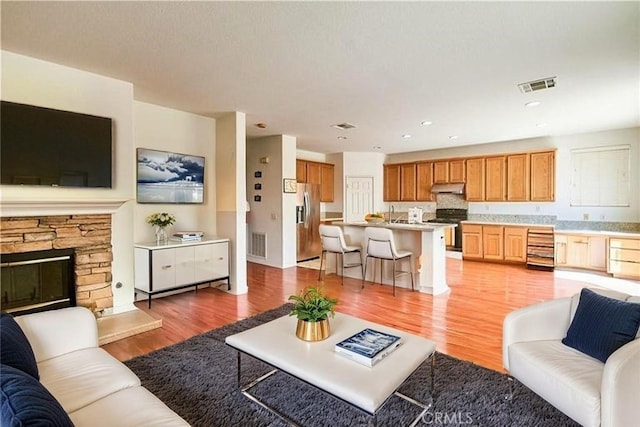 living area featuring light wood-style flooring, a stone fireplace, visible vents, and recessed lighting