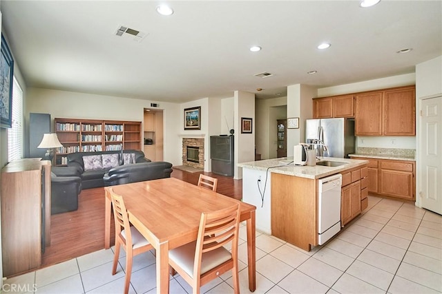 kitchen with visible vents, stainless steel refrigerator with ice dispenser, white dishwasher, an island with sink, and light tile patterned flooring